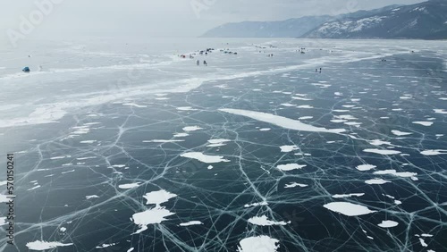 Flying a drone over tents with cars on the clear ice of Lake Baikal. Winter fishing on the largest lake