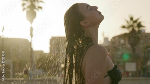 Young teen girl in heat under a stream from summer shower. Attractive woman washing under the water in the beach shower outdoors close-up. Summertime leisure. Body care. High quality 4k footage photo