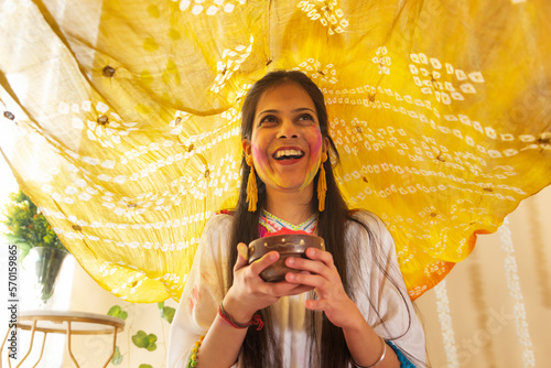 Smiling young woman with gulal on her face holding gulal bowl