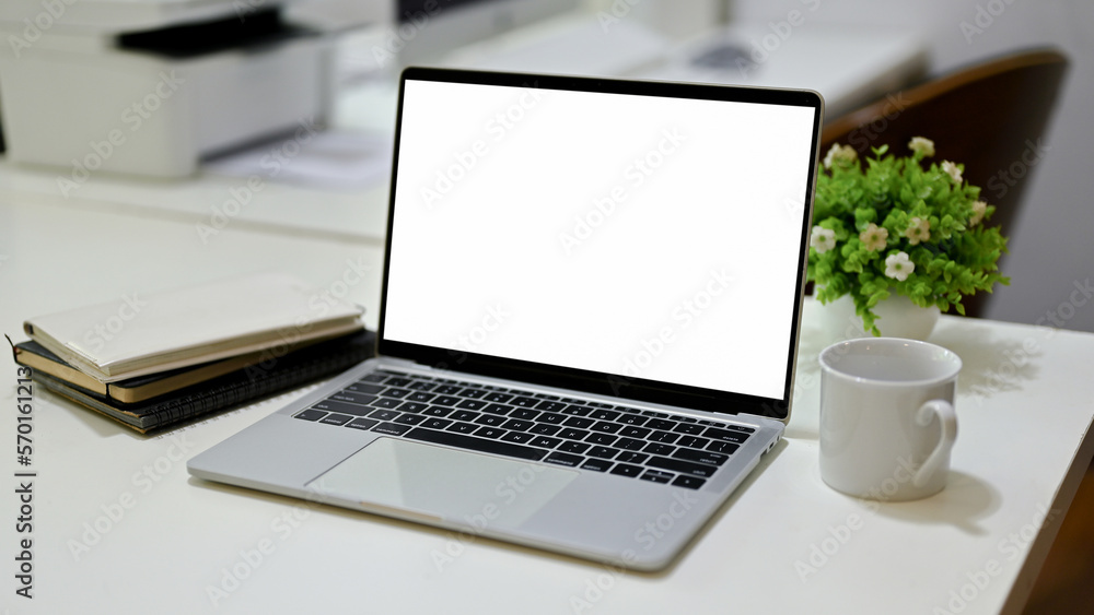 Opened laptop white screen mockup with a coffee cup, book and decor plant on office desk. Opened laptop white screen mockup with a coffee cup, book and decor plant on office desk.