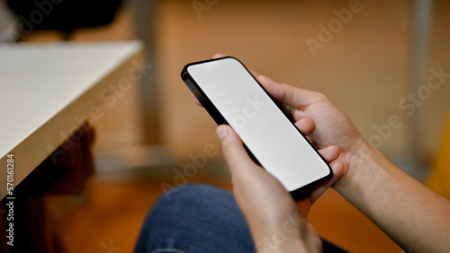 side view of a female holding a smartphone white screen mockup over blurred background.