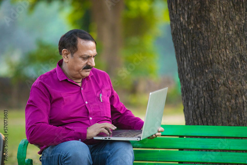 senior indian man using laptop at park.