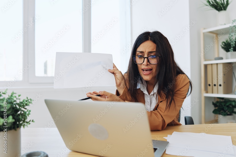 Business woman working in office at desk with laptop, anger and argument, discussing business processes online via video link, showing documents and reports Business woman working in office at desk with laptop, anger and argument, discussing business processes online via video link, showing documents and reports