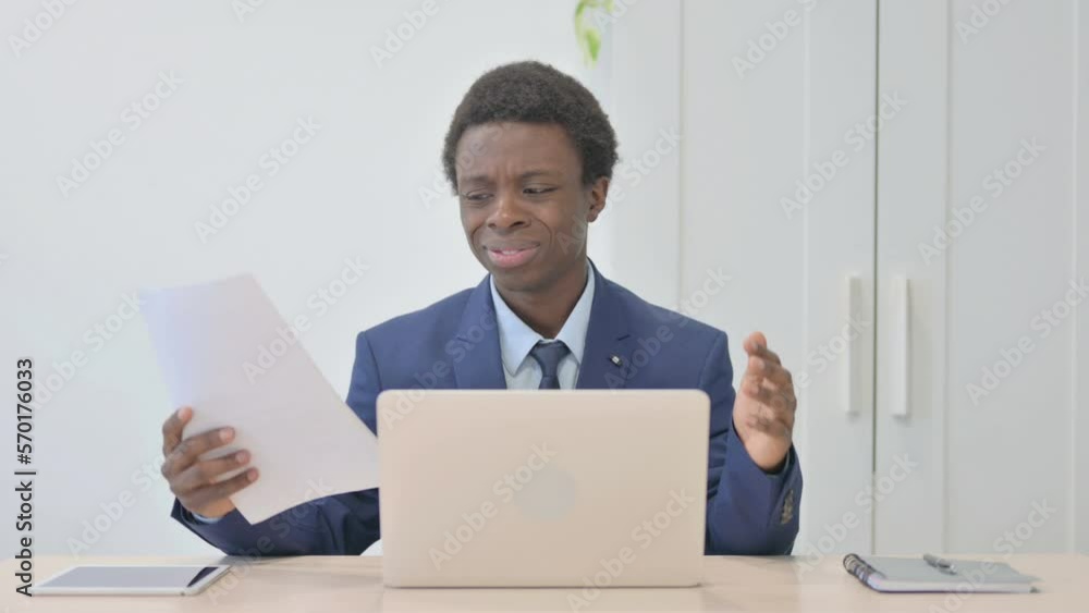Young African Businessman Facing Online Loss while Doing Paperwork Young African Businessman Facing Online Loss while Doing Paperwork