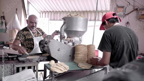 An adult man is working with his son producing corn tortillas with a nixtamall mill