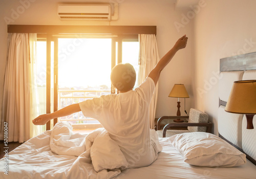 Back view woman stretching her arms in bed after wake up in the morning during sunshine shining through window 