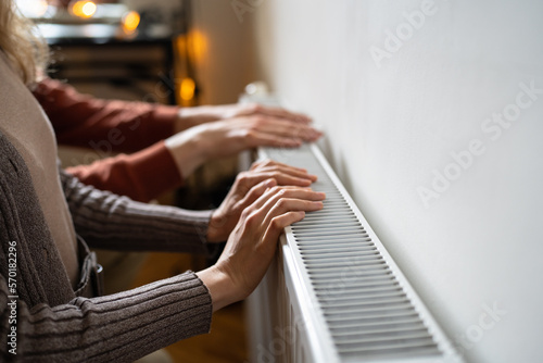Family couple touching radiator with hands, living in cold home, testing heating system while preparing house for cold weather, cropped photo. Winter energy efficiency concept