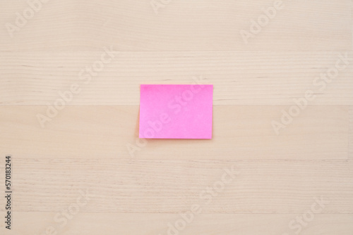 Blank pink sticky note on desk, selective focus.