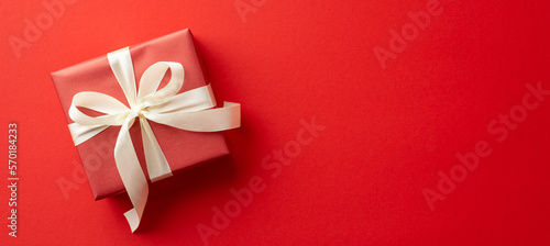 Saint Valentine's Day concept. Top view photo of giftbox with white ribbon bow on isolated red background with copyspace