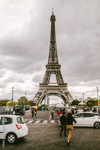 vertical retro film photo of eiffel tower with a bottom crowded of people walking and cars passing