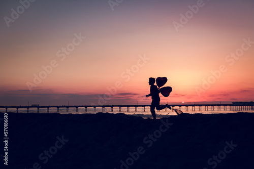 Boy running with 2 heart balloons at the beach at sunset photo