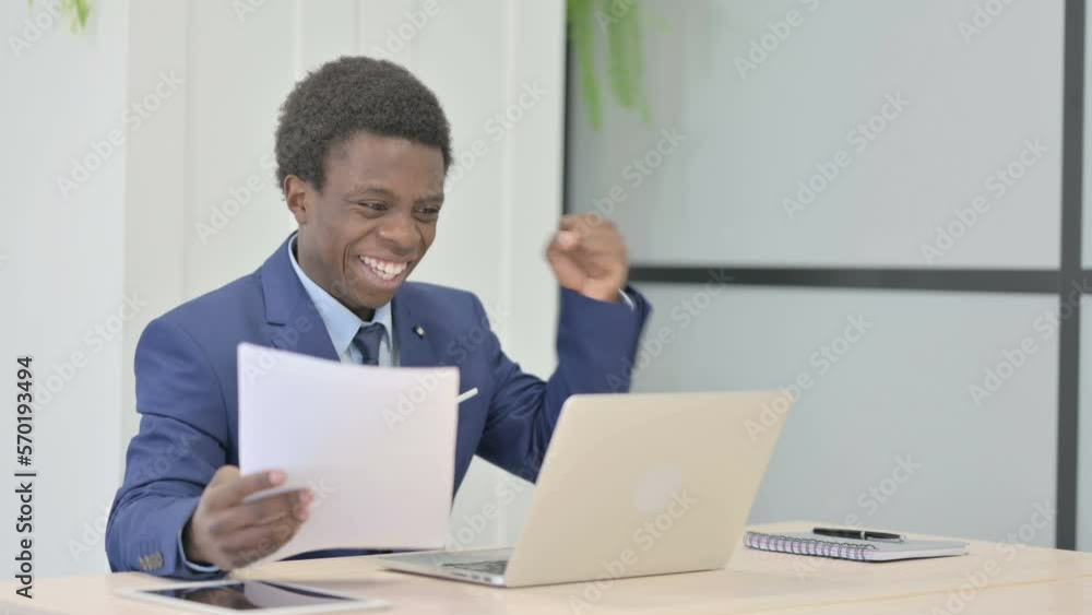 African Businessman Celebrating Success while Reading Documents in Office African Businessman Celebrating Success while Reading Documents in Office