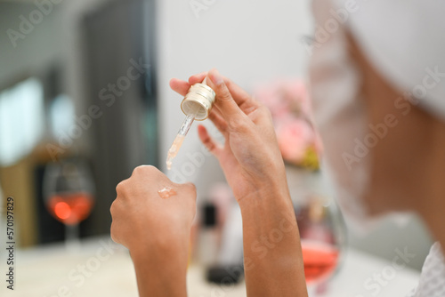 Over woman shoulder applying drop of essential oil on back of hand. Beauty treatment, skincare and cosmetics concept