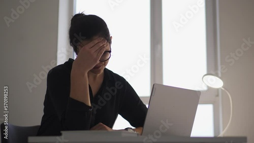Concerned young woman working on laptop in office and feeling unpleasant pain in forehead, suffering migraine and high blood pressure, overworking