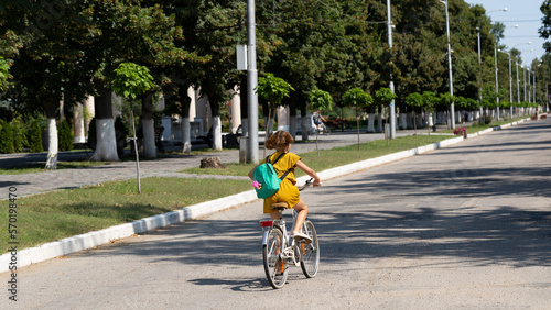A little girl rides a bicycle on the city road. View from the back.