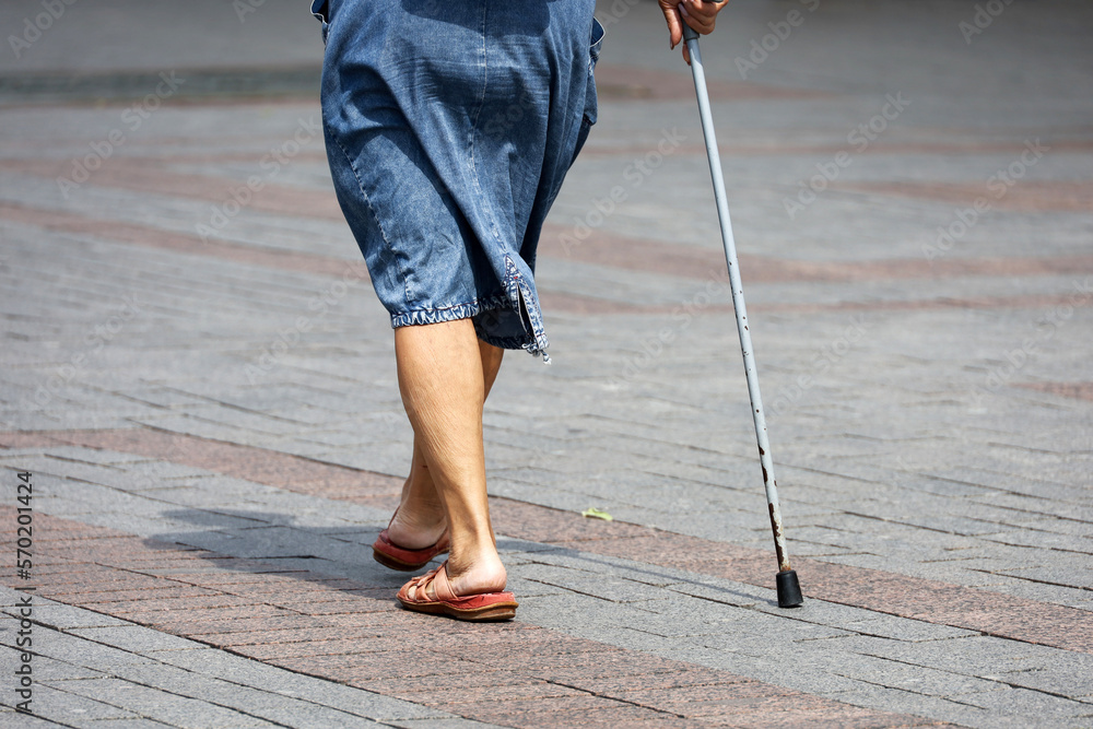 Elderly woman walking with cane on city street, legs on sidewalk