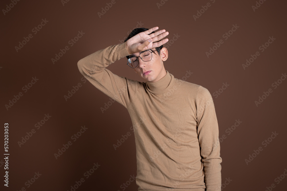Tired student holding his head. Young man on a brown background. Tired student holding his head. Young man on a brown background.