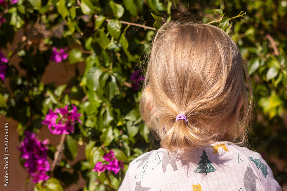 Naklejka premium Little girl with backpack standing in front of green with violet flowers