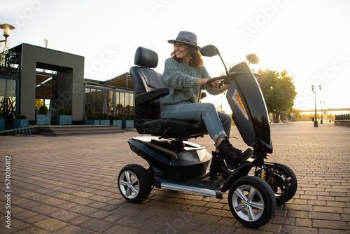 Canvas-taulu Woman tourist riding a four wheel mobility electric scooter on a city street