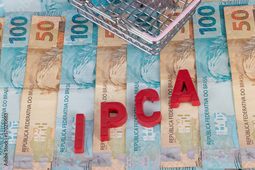Brazilian banknotes. Banknotes of 50 and 100 reais in the background with the acronym "IPCA" which in Portuguese means "Indice Nacional de Preços ao consumidor", in red. Selective focus.