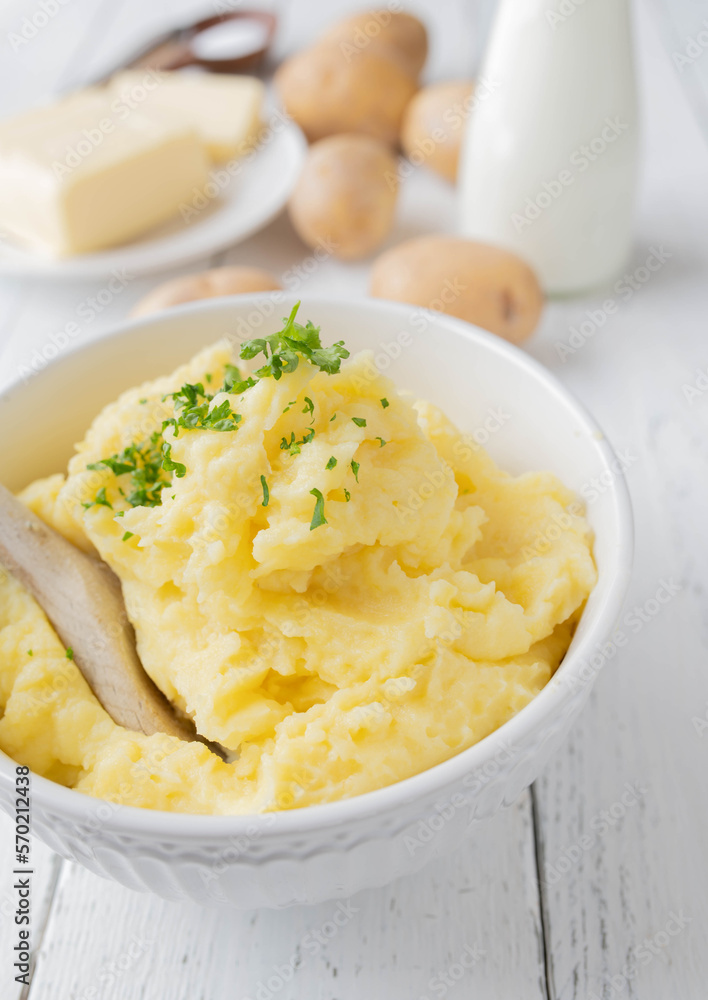 Homemade mashed potatoes in a white bowl with wooden spoon and ingredients in the background Homemade mashed potatoes in a white bowl with wooden spoon and ingredients in the background