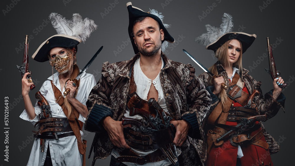 Obraz premium Studio shot of crew of corsair man and two female pirates looking at camera.