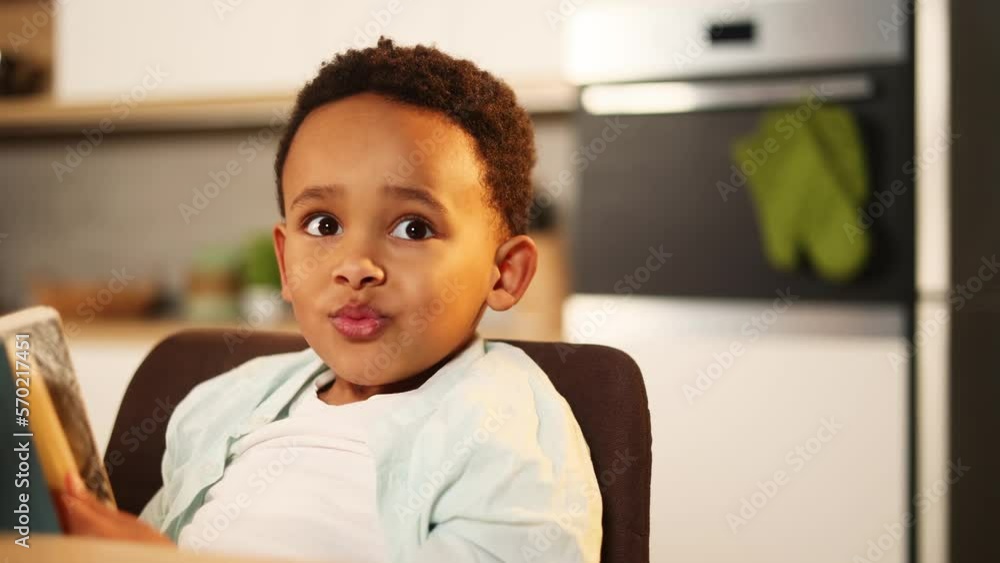 Close up portrait of cute little african american boy hold book and try to make homework while talk with his mother at home Adorable child kid prepares for school with developmental textbooks indoors Close up portrait of cute little african american boy hold book and try to make homework while talk with his mother at home Adorable child kid prepares for school with developmental textbooks indoors