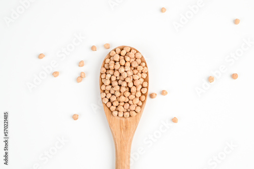 Pile of chickpeas on a wooden spoon and scattered on the white surface