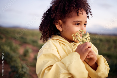 Children, farm and a girl smelling a flower outdoor in a field for agriculture or sustainability. Kids, nature and spring with a female child holding flowers to smell their aroma in the countryside photo