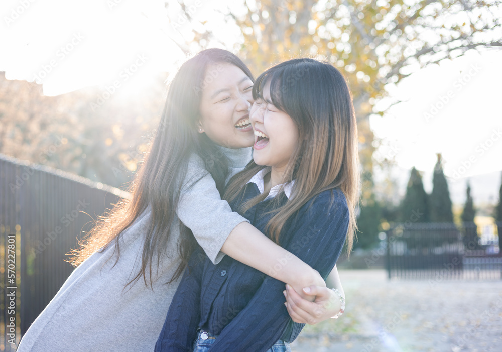 Fototapeta premium Happy lifestyle of a young Asian couple playing with each other outside. A girl pulls herself to hug the other girl to kiss her,Concept of spending time together with friends.