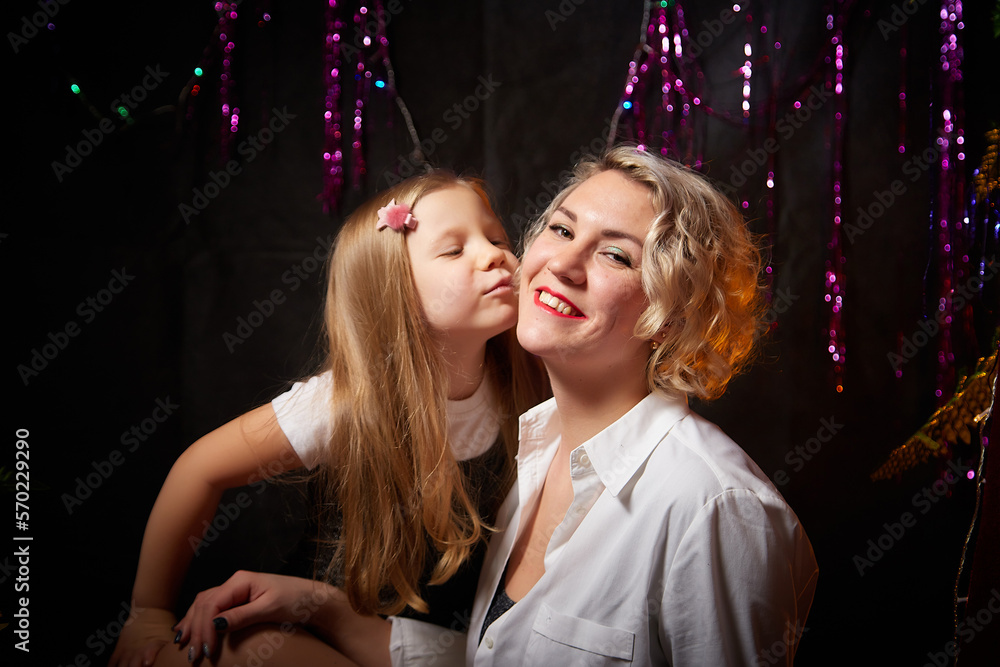 Cute mother and daughter in a room decorated for Christmas. The tradition of decorating the house and dressing up for the holidays. Happy childhood and motherhood