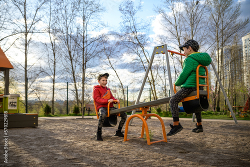 Two little kid boys having fun with swing on outdoor playground. Children, best friends and siblings swinging on warm sunny spring or autumn day. Active leisure with kids. Casual boy fashion