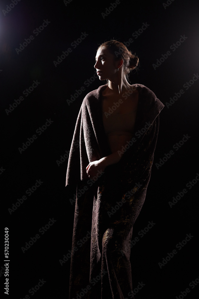 The silhouette of a girl in a veil looking like a statue or sculpture on a black background. A model poses for a photo shoot in the studio The silhouette of a girl in a veil looking like a statue or sculpture on a black background. A model poses for a photo shoot in the studio