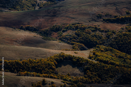 Photo of a scenic view of hills under sunlight and clouds shadows from the plateau Bermamyt. There are beautiful trees in autumn colors on the hills.