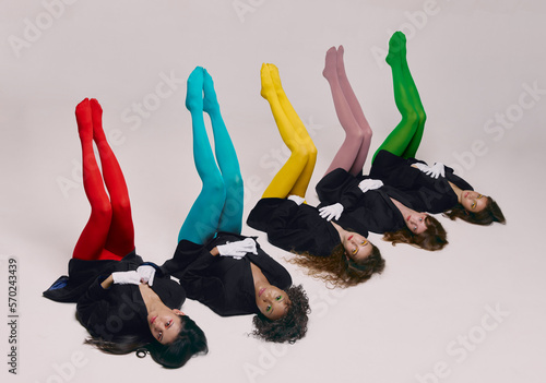 Legs up. Portrait of young beautiful women in black jackets and colored tights lying on floor over grey background. Concept of contemporary art, fashion photo