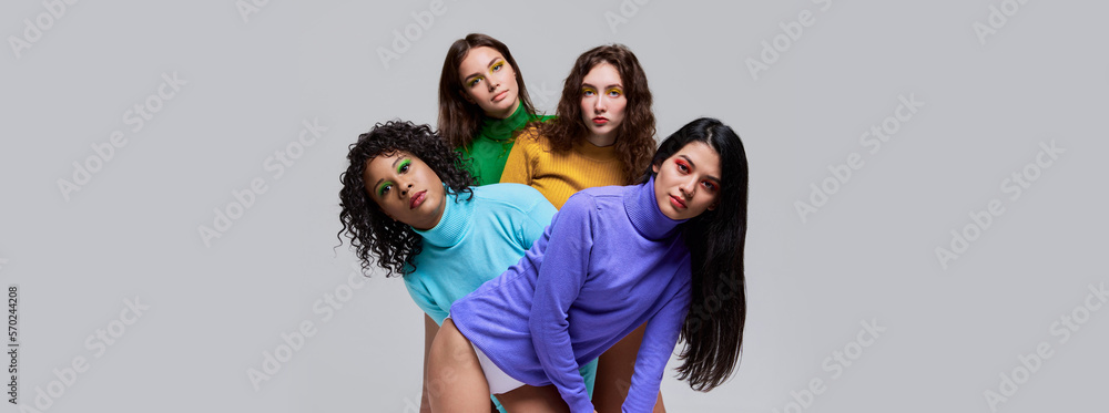 Young beautiful women with distant glance wearing multicolored sweaters posing over grey background. Concept of diversity, beauty, extraordinary fashion, modern style, youth Young beautiful women with distant glance wearing multicolored sweaters posing over grey background. Concept of diversity, beauty, extraordinary fashion, modern style, youth