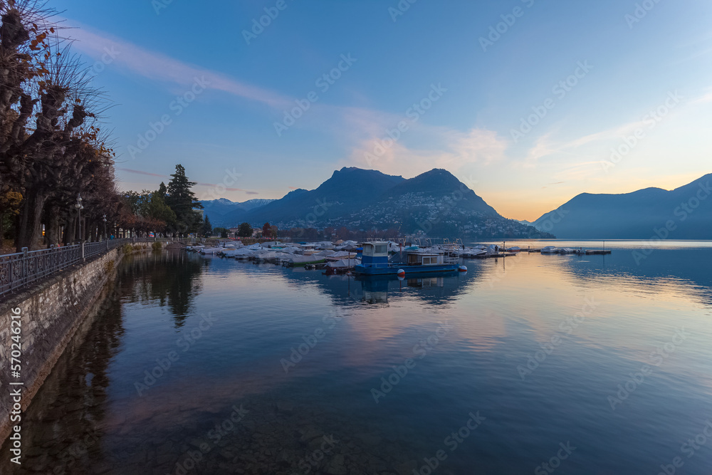 Sunrise panorama of Lugano lake in autumn early morning with mooring for pleasure boats. Lugano, Ticino, Switzerland