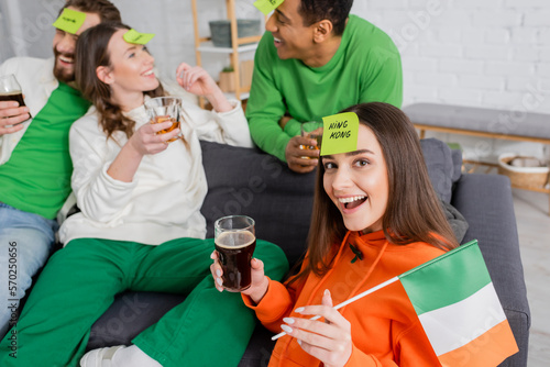 excited woman with king king word on sticky note holding Irish flag and glass of beer near interracial friends on Saint Patrick Day