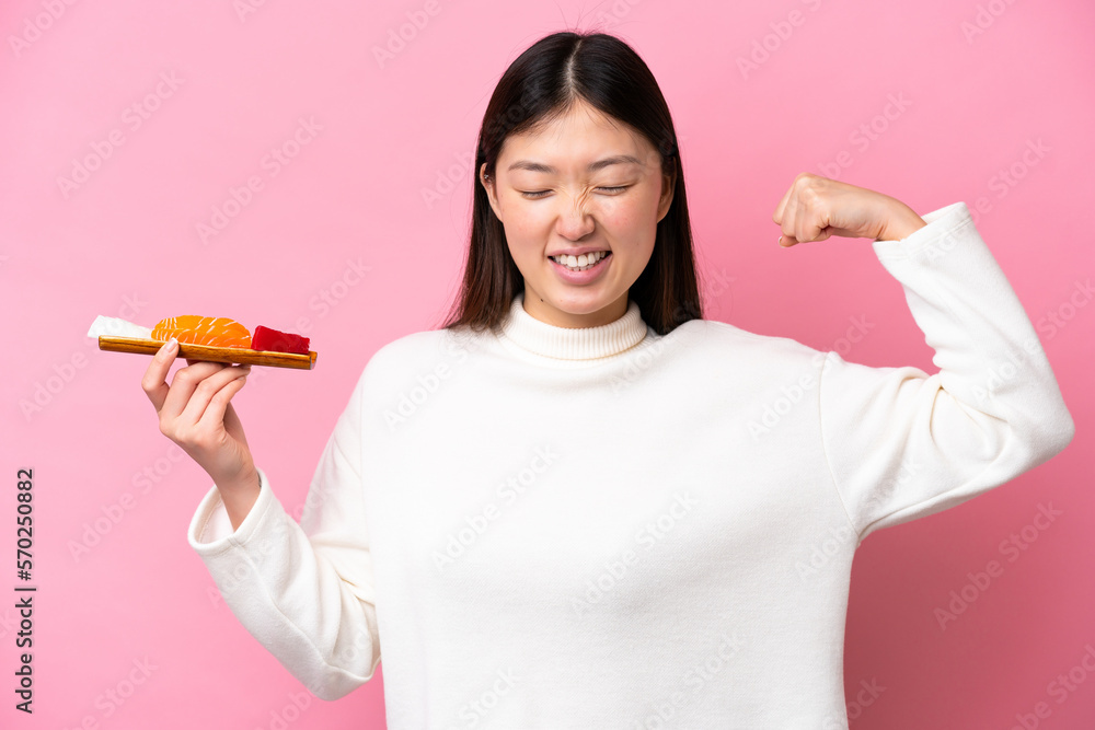 Young Chinese woman holding sashimi isolated on pink background doing strong gesture Young Chinese woman holding sashimi isolated on pink background doing strong gesture
