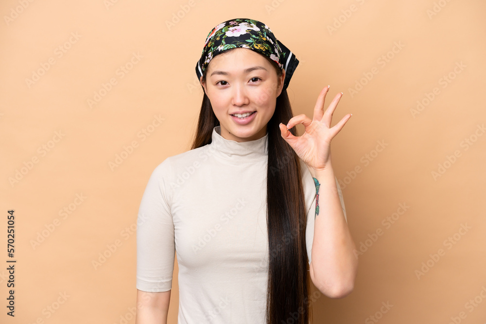 Young Chinese woman isolated on beige background showing ok sign with fingers