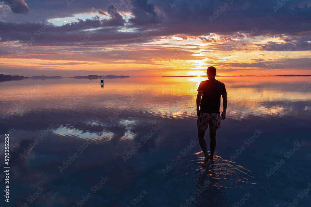 Silhouette of man walking into the sunrise of lake Bonneville Salt Flats, Wendover, Western Utah, USA, America. Dreamy red colored clouds mirroring on the water surface creating romantic atmosphere Silhouette of man walking into the sunrise of lake Bonneville Salt Flats, Wendover, Western Utah, USA, America. Dreamy red colored clouds mirroring on the water surface creating romantic atmosphere