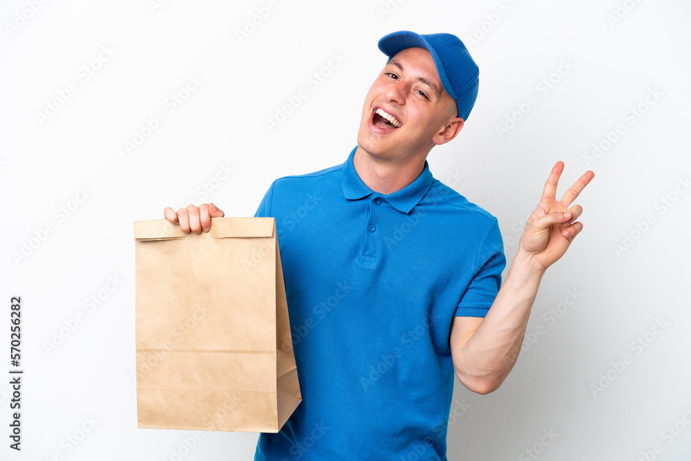 Young Brazilian man taking a bag of takeaway food isolated on white background smiling and showing victory sign Young Brazilian man taking a bag of takeaway food isolated on white background smiling and showing victory sign