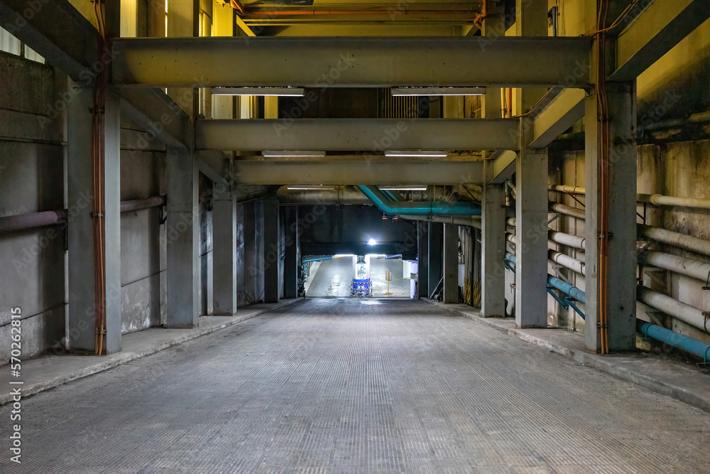 Entrance to an underground car park at night. Yellow metal girders, gray asphalt and lighting. Empty scene with no cars or people