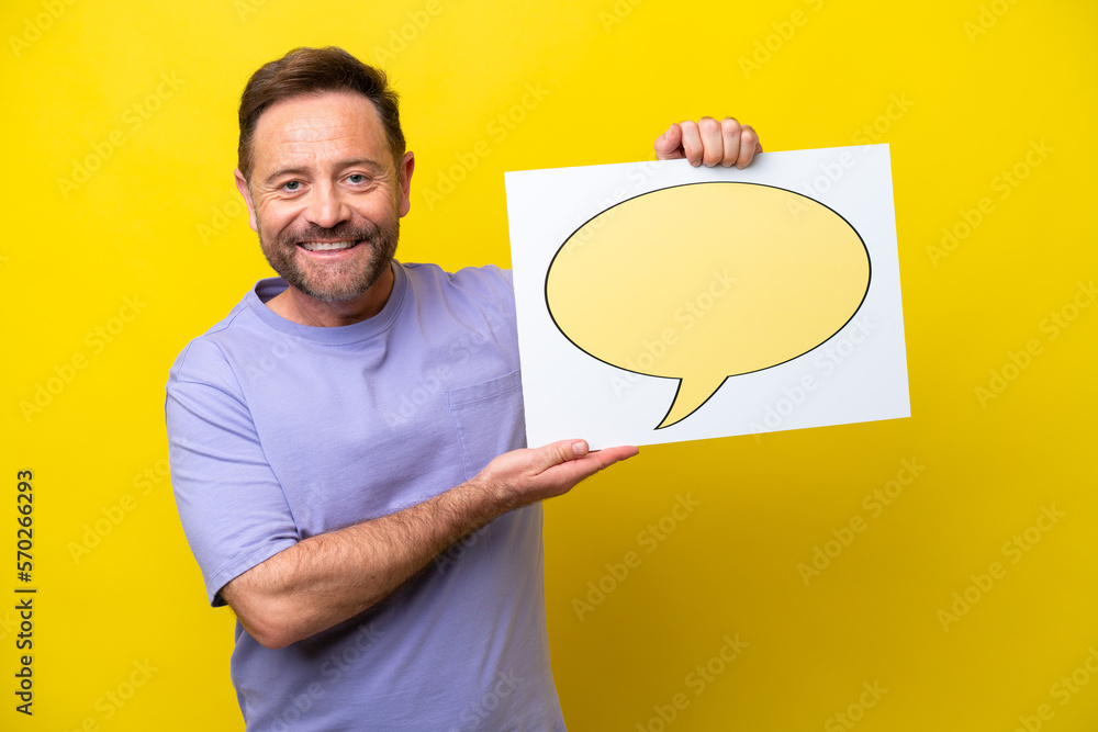 Middle age caucasian man isolated on yellow background holding a placard with speech bubble icon and pointing it Middle age caucasian man isolated on yellow background holding a placard with speech bubble icon and pointing it