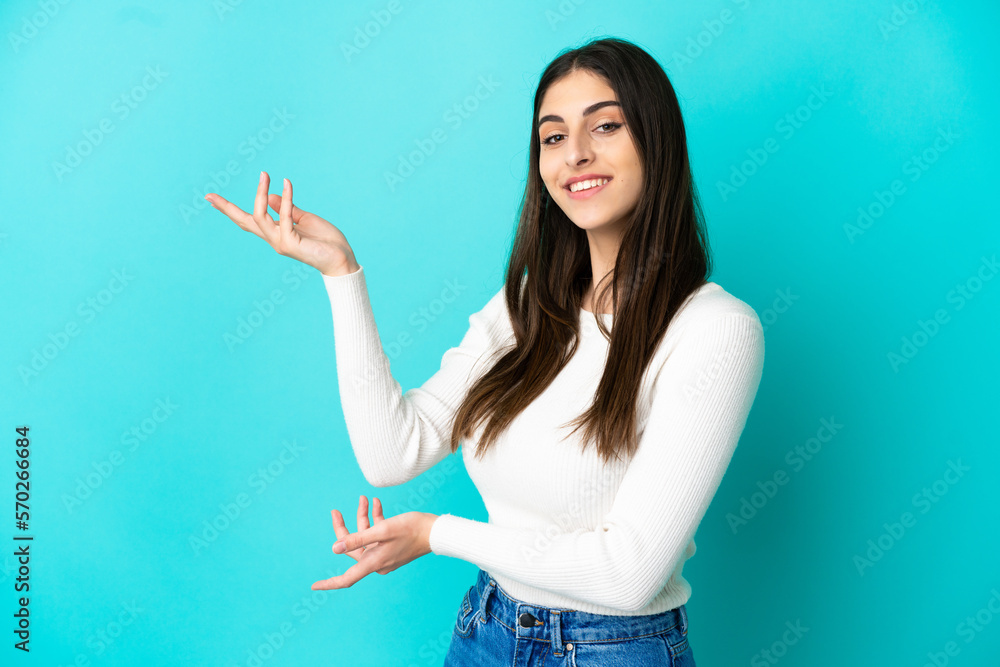 Young caucasian woman isolated on blue background extending hands to the side for inviting to come Young caucasian woman isolated on blue background extending hands to the side for inviting to come