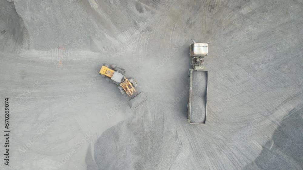 Sand loaders are shoveling rocks into dump trucks.
