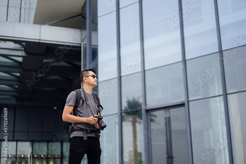 man taking photo during travel. Traveler man with camera and backpack outdoor. Young tourist male taking memory pic. Travel Asian man backpack taking