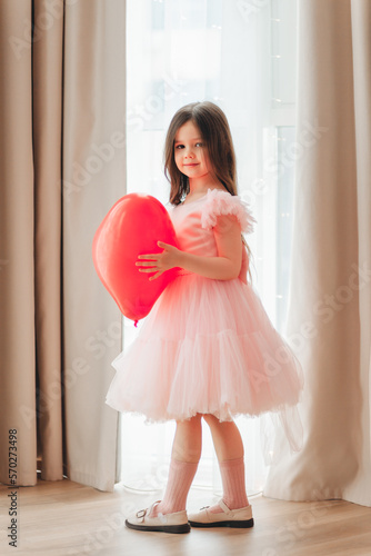 valentine's day baby. A little girl in a red dress holds a large ball in the shape of a heart