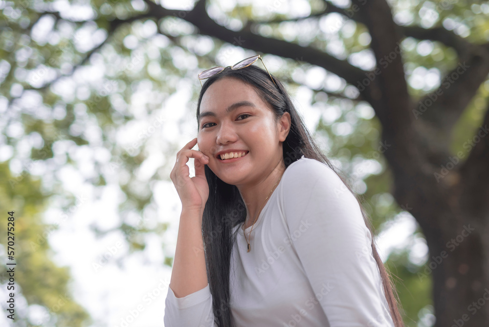 A lovely young woman poses for the camera with a big smile on her face for a low angle shot with trees background. A lovely young woman poses for the camera with a big smile on her face for a low angle shot with trees background.