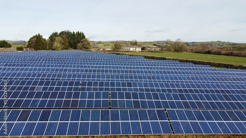 Solar panel farm low aerial view with copy space. A fields full of solar panels sit in a green grassy field producing clean zero carbon energy. Solar energy production. Solar panel farm low aerial view with copy space. A fields full of solar panels sit in a green grassy field producing clean zero carbon energy. Solar energy production.